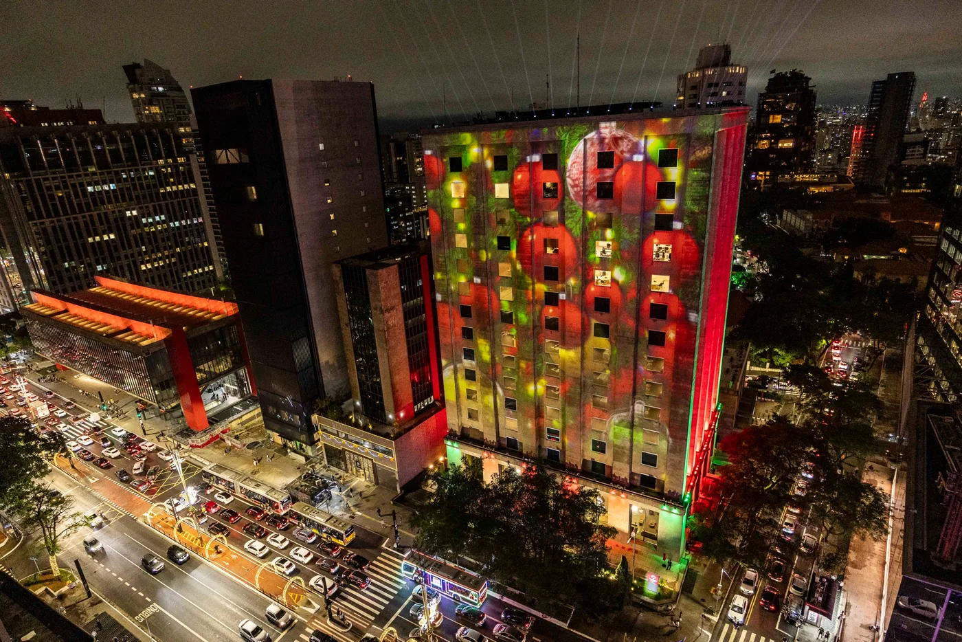 A mesma fachada com projeção em grid verde e vermelho, em que cada janela do edifício funciona como um pixel do desenho natalino