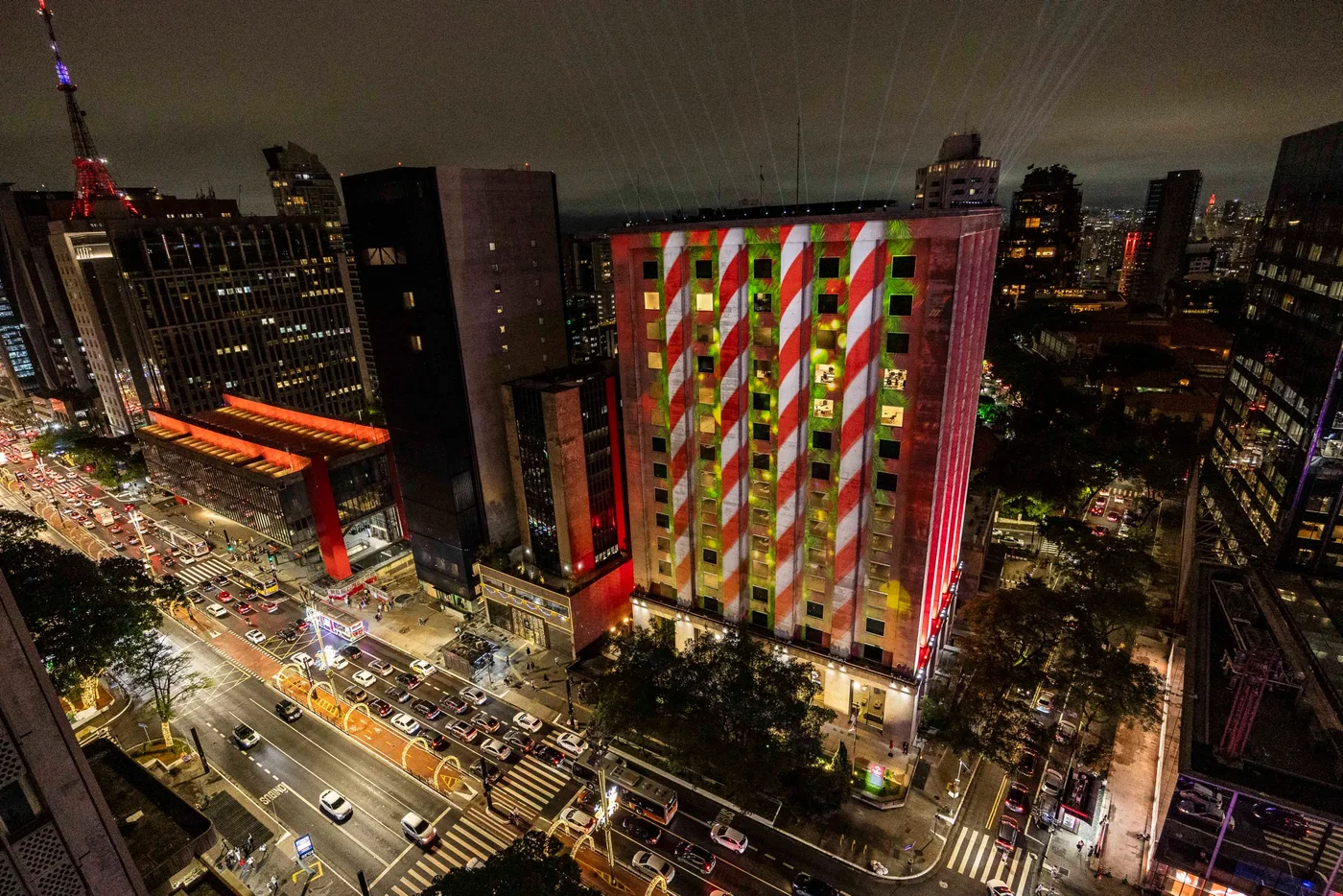 A fachada projetada em listras verticais verdes e vermelhas, no padrão de bengala doce, com a Avenida Paulista movimentada ao pé do prédio